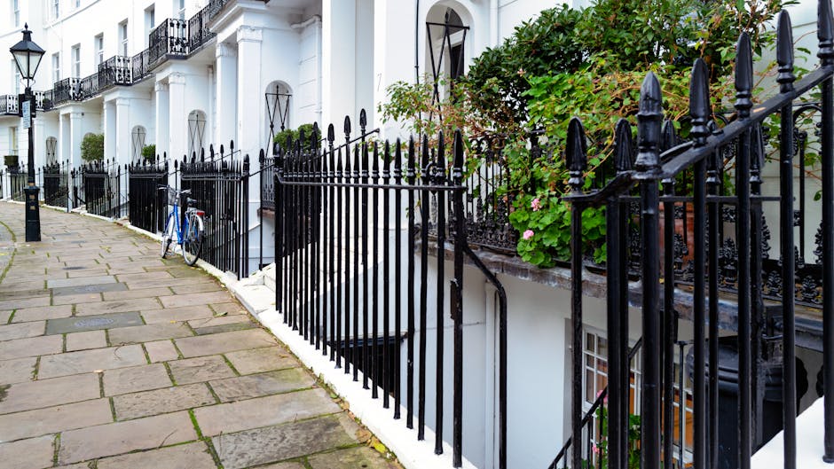 A row of white terraced houses with black wrought iron railings lining the pavement outside, featuring decorative finials and mounted on stone bases. In the foreground, a blue bicycle is parked agains